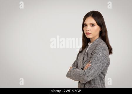 Giovane donna sicura di sé con un blazer a quadri, braccia incrociate Foto Stock