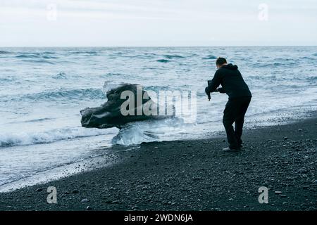 Diamond Beach, Islanda - 7 luglio 2023: L'uomo scatta foto di un grande pezzo di ghiaccio a Diamond Beach Islanda Foto Stock