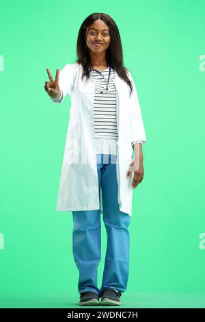 Una dottoressa, su sfondo verde, a piena altezza, mostra un segno di vittoria Foto Stock