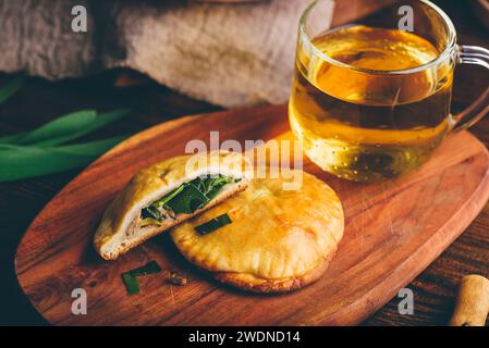 Dolci al forno ripieni di erba cipollina siberiana e funghi con tazza di tè verde su vassoio di legno Foto Stock