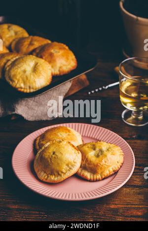 Pasticceria appena sfornata ripiena di erba cipollina e funghi su piatto e bicchiere di vino bianco Foto Stock