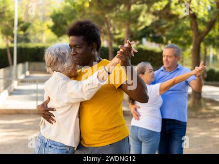 Felici i pensionati multinazionali maturi che trascorrono il tempo insieme e ballano in coppia all'aperto Foto Stock