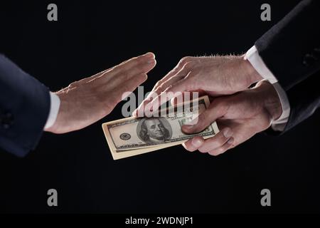 La mano di un uomo in un vestito nero tiene fuori un wad di soldi, che rifiuta. Concetto di Giornata Mondiale contro la corruzione Foto Stock