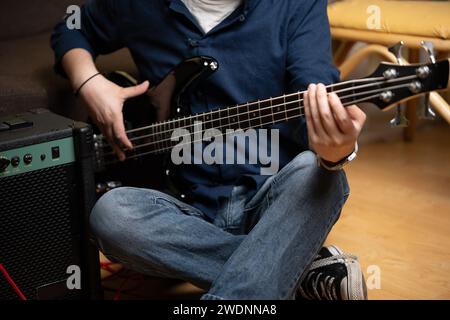 uomo latino che impara a suonare bassi elettrici a casa accanto a un amplificatore Foto Stock