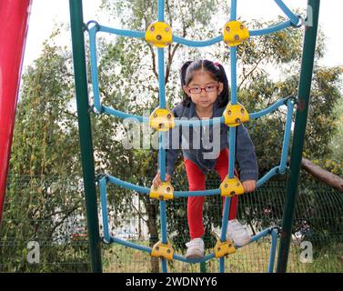 Una bruna latina di 4 anni gioca in un parco giochi, svolge attività fisica come terapia ADHD, vivendo in povertà Foto Stock