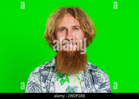 Allegro, bello, felice, giovane uomo caucasico sorridente, amichevole, felice espressione che guarda la macchina fotografica sognare, riposare, rilassarsi sentirsi soddisfatti buone notizie. Uomo con barba rossa su sfondo cromatico verde Foto Stock