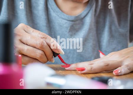 Giovane donna ispanica che dipinge le unghie con un colore rosso sul tavolo. Utilizza lucidi per unghie semipermanenti che deve asciugare alla luce UV. Foto Stock