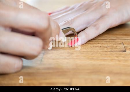 Mani da donna con pinzette per l'applicazione dell'accessorio per unghie. Sta applicando un po' di glitter rosso sull'unghia. Foto Stock