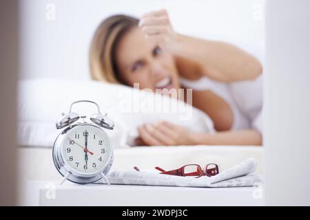 Dormire, rabbia e donna a letto con sveglia per dormire, svegliarsi e fare la routine mattutina a casa. Pigro, stanco e frustrato, arrabbiato e turbato Foto Stock