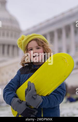 I bambini giocano con lo snowboard nel parco invernale. Prima neve invernale. I bambini svernano le vacanze. Bambino felice che gioca con la neve nel parco invernale. Portrait Kid Throw Foto Stock