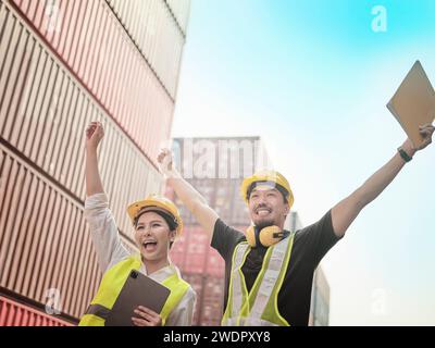 Due ingegneri asiatici alzano le mani per la vittoria, missione completa, sorridono per mostrare la loro felicità in Container Terminal. Foto Stock