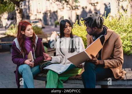 Tre studenti diversi sono profondamente impegnati in una sessione di studio di gruppo all'esterno, condividendo idee e imparando insieme. Foto Stock