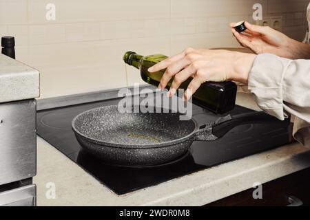 Donna irriconoscibile che versa olio d'oliva sulla padella dal biberon Foto Stock