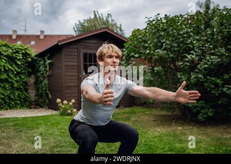 Uomo di mezza età che si esercita all'aperto in giardino, facendo squat. Concetto di routine di allenamento a casa. Foto Stock