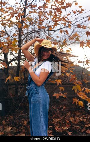 Giovane donna che gira tenendo il cappello davanti all'albero in autunno Foto Stock