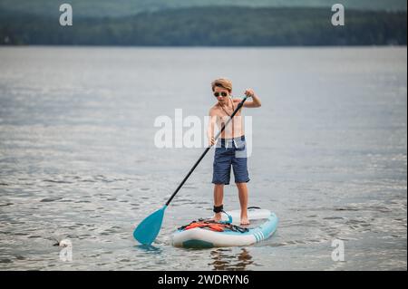 Tween ragazzo con occhiali da sole paddle boarding Foto Stock