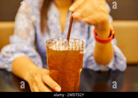 Parte centrale di una donna che tiene un tè ghiacciato al ristorante Foto Stock