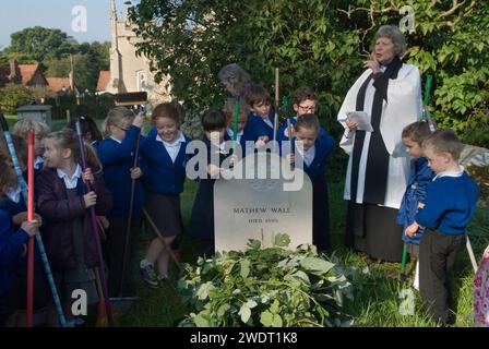 Braughing, Hertfordshire, Inghilterra 1 ottobre 2015. Old Mans Day, il Rev'd Julie Gawthrope con bambini della Jenyns First School intorno alla tomba di Mathew Wall. Brambles è stato posto sulla tomba come indicato nel suo testamento per evitare che il bestiame pascoli sopra di essa. Un breve servizio viene tenuto mentre le campane della chiesa suonano per un funerale, e poi viene suonata una buccia nuziale. Foto Stock