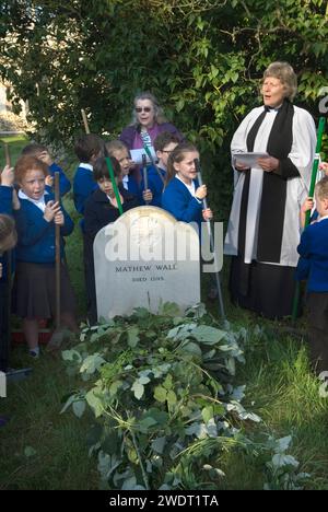 Braughing, Hertfordshire, Inghilterra 1 ottobre 2015. Old Mans Day, il reverendo Julie Gawthrope e i bambini della Jenyns First School intorno alla tomba di Mathew Wall. Brambles è stato posto sulla tomba come indicato nel suo testamento per evitare che il bestiame pascoli sopra di essa. Un breve servizio viene tenuto mentre le campane della chiesa suonano per un funerale, e poi viene suonata una buccia nuziale. Foto Stock