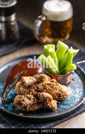 Cosce di pollo fritte con bastoncini di sedano e birra alla spina al piatto nel pub o nel ristorante. Foto Stock