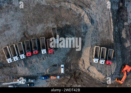Vista aerea dall'alto verso il basso dell'escavatore e dei dumper da scarico durante i lavori di terra in cantiere. Industria edile Foto Stock