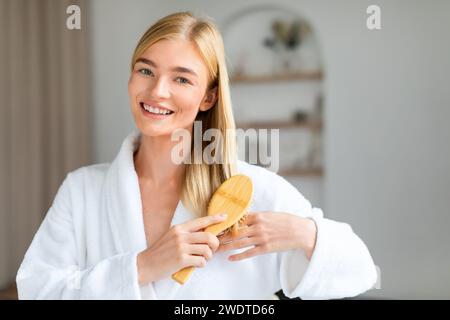 Signora bionda che si prende cura dei capelli lunghi e lisci in casa Foto Stock
