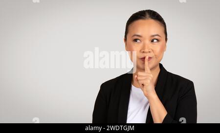 Donna d'affari asiatica con un dito sulle labbra che fa un gesto di silenzio Foto Stock