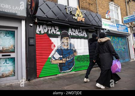 Londra, Regno Unito. 21 gennaio 2024. I membri del pass pubblico illustrano un'immagine del giornalista palestinese Motaz Azaiza su una bandiera palestinese dipinta su un negozio cieco a Tower Hamlets. Ci sono molti simboli visibili di solidarietà con i palestinesi nella zona di Tower Hamlets di Londra, tra cui Street art pro-palestinese prodotta da Paint for Palestine e bandiere palestinesi. Crediti: Mark Kerrison/Alamy Live News Foto Stock