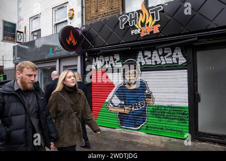 Londra, Regno Unito. 21 gennaio 2024. I membri del pass pubblico illustrano un'immagine del giornalista palestinese Motaz Azaiza su una bandiera palestinese dipinta su un negozio cieco a Tower Hamlets. Ci sono molti simboli visibili di solidarietà con i palestinesi nella zona di Tower Hamlets di Londra, tra cui Street art pro-palestinese prodotta da Paint for Palestine e bandiere palestinesi. Crediti: Mark Kerrison/Alamy Live News Foto Stock