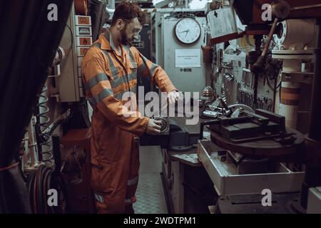 Giovane ingegnere meccanico che ripara parti del motore, fissato in morsa in officina, indossando tute e occhiali di protezione. Foto Stock