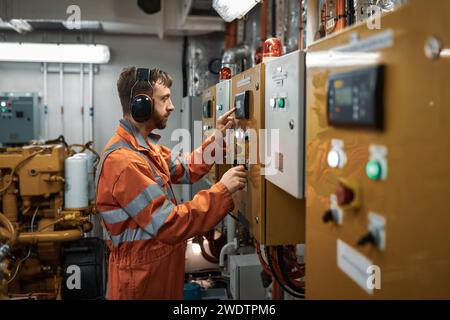 Giovane ufficiale ingegnere che avvia manualmente il generatore diesel nella sala macchine. Foto Stock