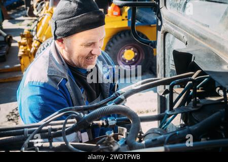 Riparazione meccanica del motore del trattore o dell'attrezzatura pesante. L'agricoltore ispeziona e diagnostica le macchine agricole. Foto Stock