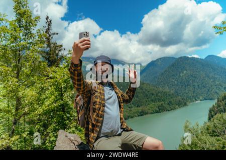 Viaggiatore escursionistico bell'uomo con barba caucasica con zaino che scatta selfie contro la vista del lago Ritsa in Abkhazia Foto Stock