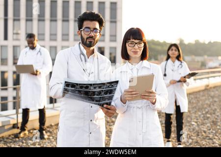 Donna caucasica con compressa in camice da laboratorio e giovane medico maschio barbato. Foto Stock