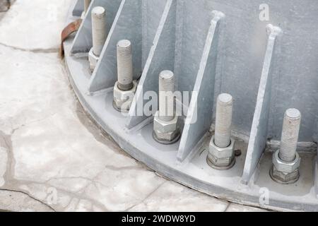 Bulloni e dadi su una piastra di acciaio. Diverse coppie di bulloni argentati sono fissati saldamente sulla base rotonda in metallo della colonna alla base in calcestruzzo del con Foto Stock