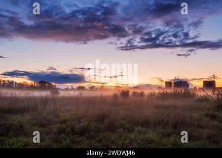 Misty Field sullo sfondo di un bellissimo cielo nuvoloso al tramonto. Splendido paesaggio urbano in una serata nebbiosa. Foto Stock