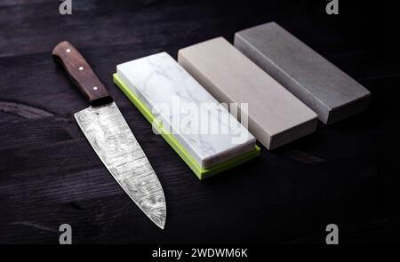 Il coltello da cucina Big Kitchen si appoggia sul tavolo da cucina, accompagnato da un set di pietre per affilare, il tutto su sfondo nero Foto Stock