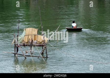Fisherman on basket boat o thung chai - barca arrotondata in bambù, con capanna da pesca sfocata sulla sinistra in Vietnam Foto Stock