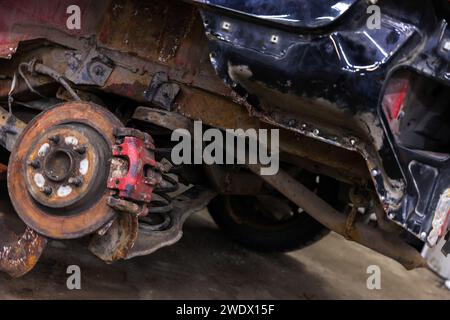 Foto ravvicinata del disco del freno e della sospensione di una vecchia vettura rotta dopo un incidente stradale Foto Stock