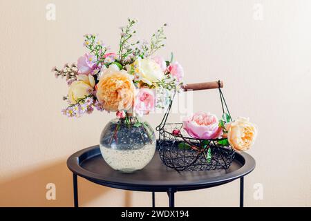 Bouquet fresco di fiori di rose messo in vaso di vetro su tavola. Primo piano di fiori gialli rosa con cesto. Arredamento estivo Foto Stock