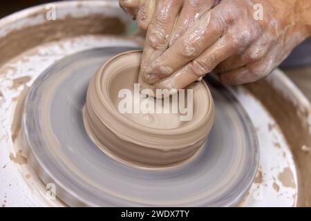 Mani maschili che creano una tazza sulla ruota in ceramica, primo piano Foto Stock