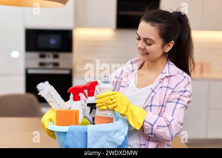 Donna in guanti protettivi di gomma gialli che tiene il secchio con detergenti e stracci per la pulizia . faccende domestiche. Foto Stock