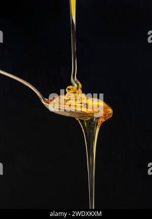 Miele che cade su un cucchiaio isolato su sfondo nero Foto Stock