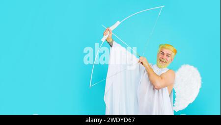 San Valentino. L'angelo di San Valentino maschio spara una freccia d'amore. Uomo barbato sorridente in costume d'angelo che mira con l'arco. San Valentino cupido in ali d'angelo Foto Stock