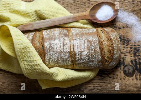 pane fresco con cucchiaio di legno e sale, panno, su fondo di legno. Foto Stock