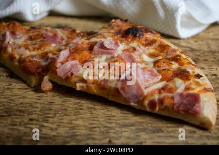 pizza al forno su un tavolo di legno e un panno bianco sullo sfondo - triangolo per pizza. Foto Stock