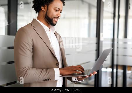 Concentrato e diligente, un uomo d'affari che digita il notebook sullo sfondo di un ufficio contemporaneo, evidenziando il suo impegno per la produttività e la moderna gestione aziendale Foto Stock