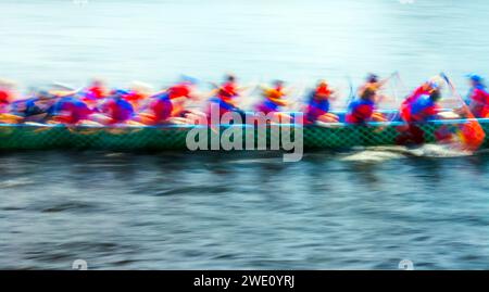 Dragon boat che gareggia in una gara dinamica e sfocata mentre i concorrenti remono lungo il fiume Foto Stock