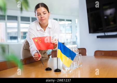 La giovane donna fissa bandiere in miniatura di Ucraina e Cina per i negoziati internazionali Foto Stock