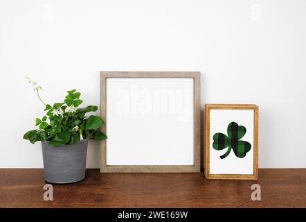 Montatura in legno con decorazioni St Patricks Day su un ripiano in legno. Pianta di Shamrock e cartello di legno di tessuto a quadri. Cornice quadrata contro una parete bianca. Copia spac Foto Stock